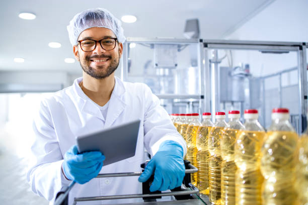 oil Portrait of an experienced technologist worker standing in food factory. In background automated conveyor machine with bottled sunflower oil.